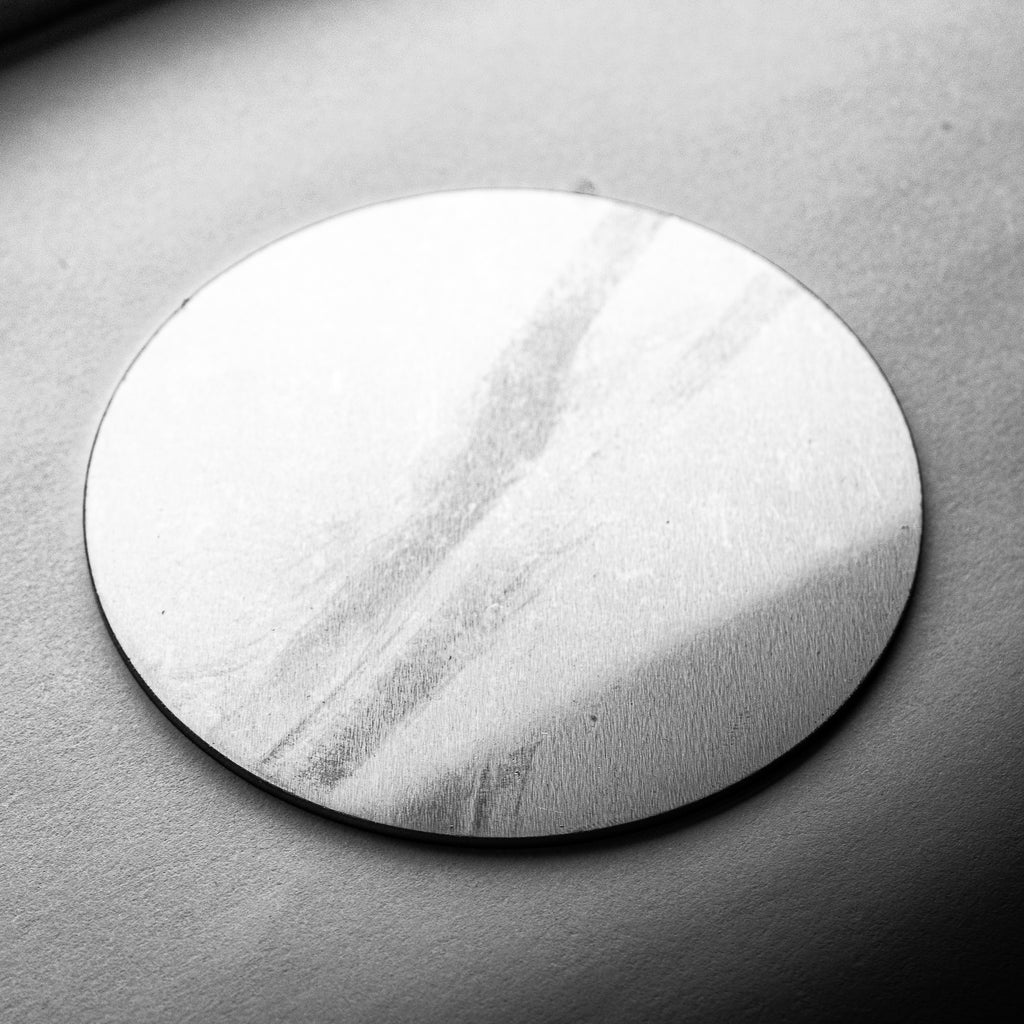Round stainless steel blank badge on a gray surface